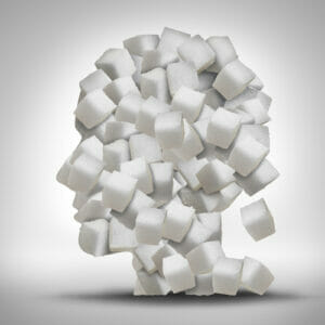 Sugar addiction concept as a human head made of white granulated refined sweet cubes as a health care symbol for being addicted to sweeteners and the medical issues pertaining to processed food.